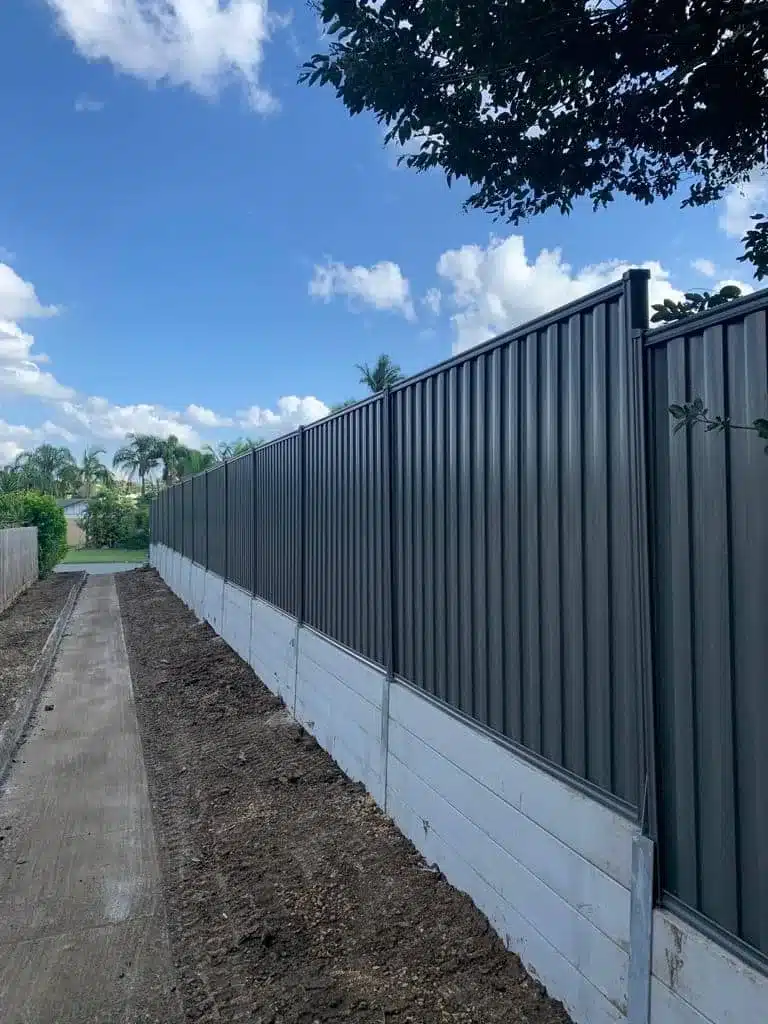 Concrete sleeper retaining wall below a green Colorbond fence along a side path