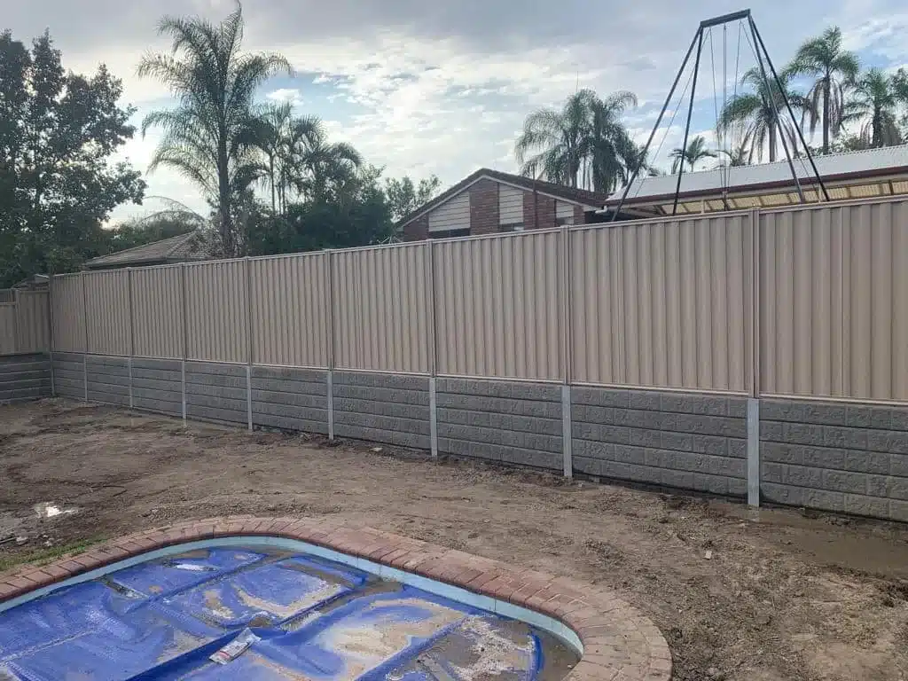 Grey concrete sleeper retaining wall beneath a beige Colorbond fence in a backyard