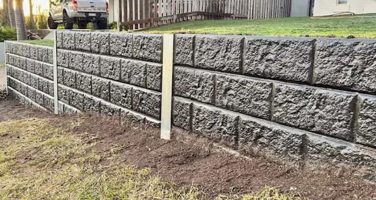 Rock-face concrete sleeper retaining wall along a freshly prepared garden bed