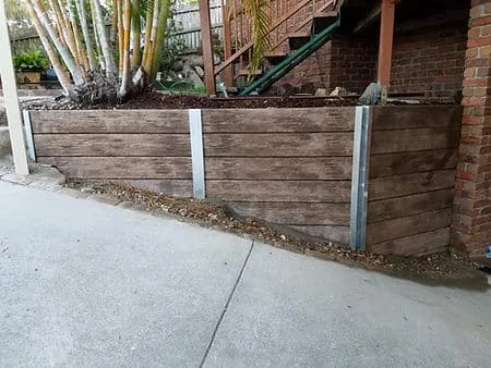 Timber sleeper retaining wall with steel posts beside a concrete driveway
