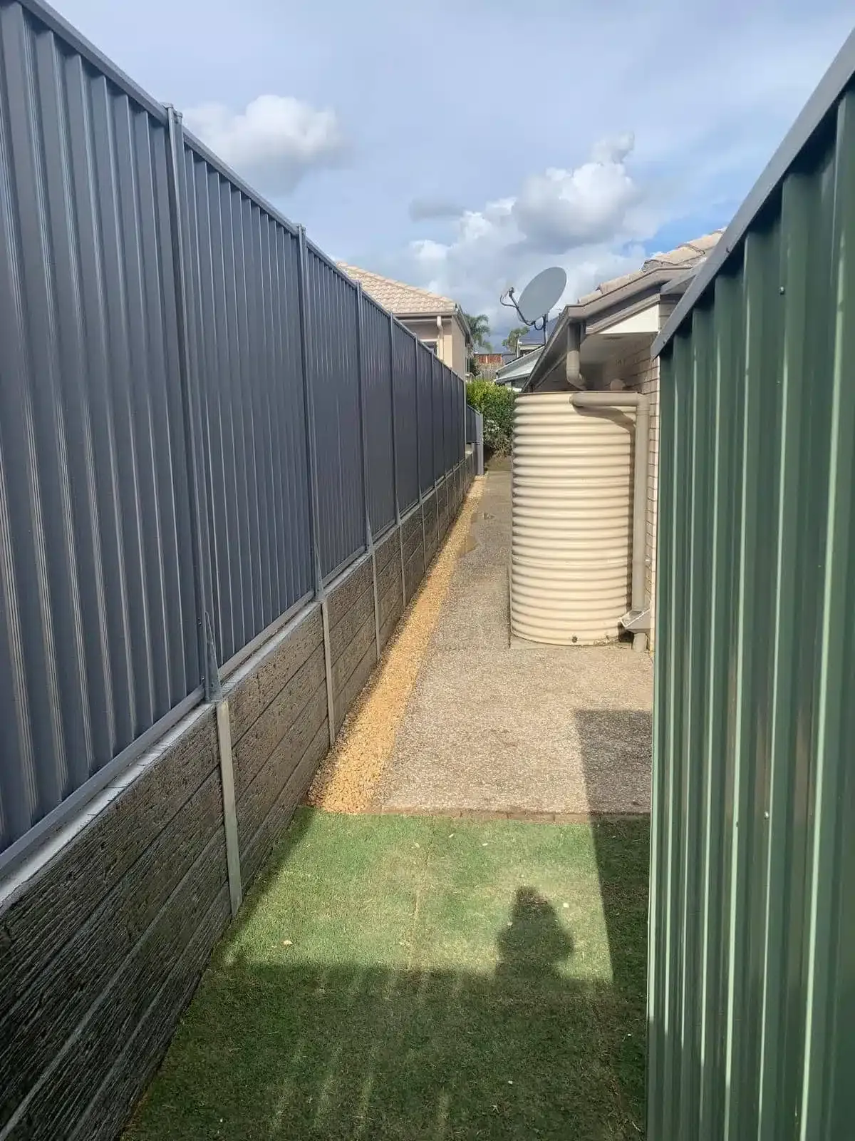 Concrete sleeper retaining wall along a side path between Colorbond fences