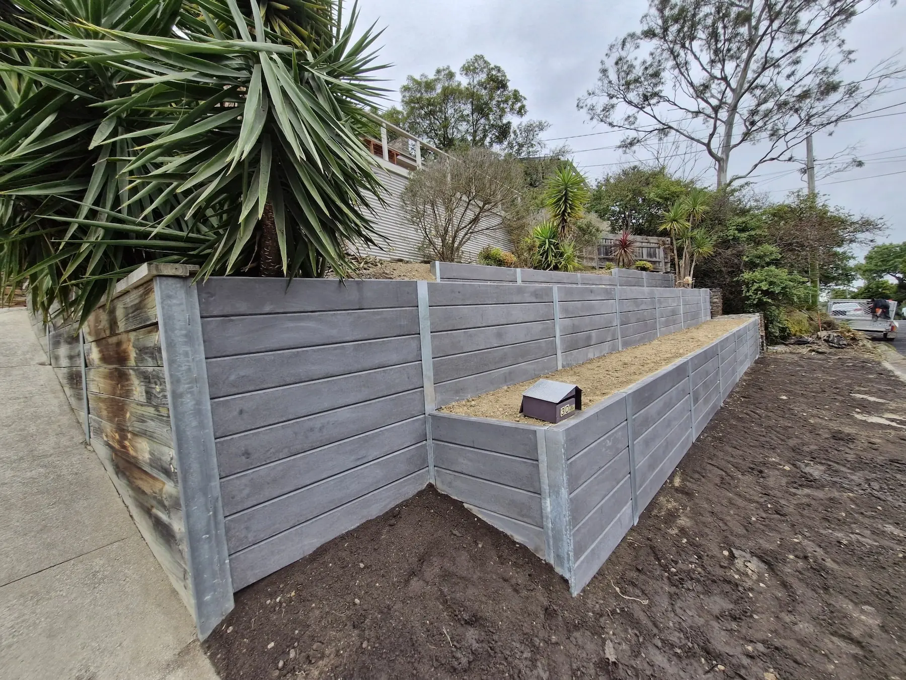 Grey concrete sleeper retaining wall wrapping around a corner garden bed beside a driveway