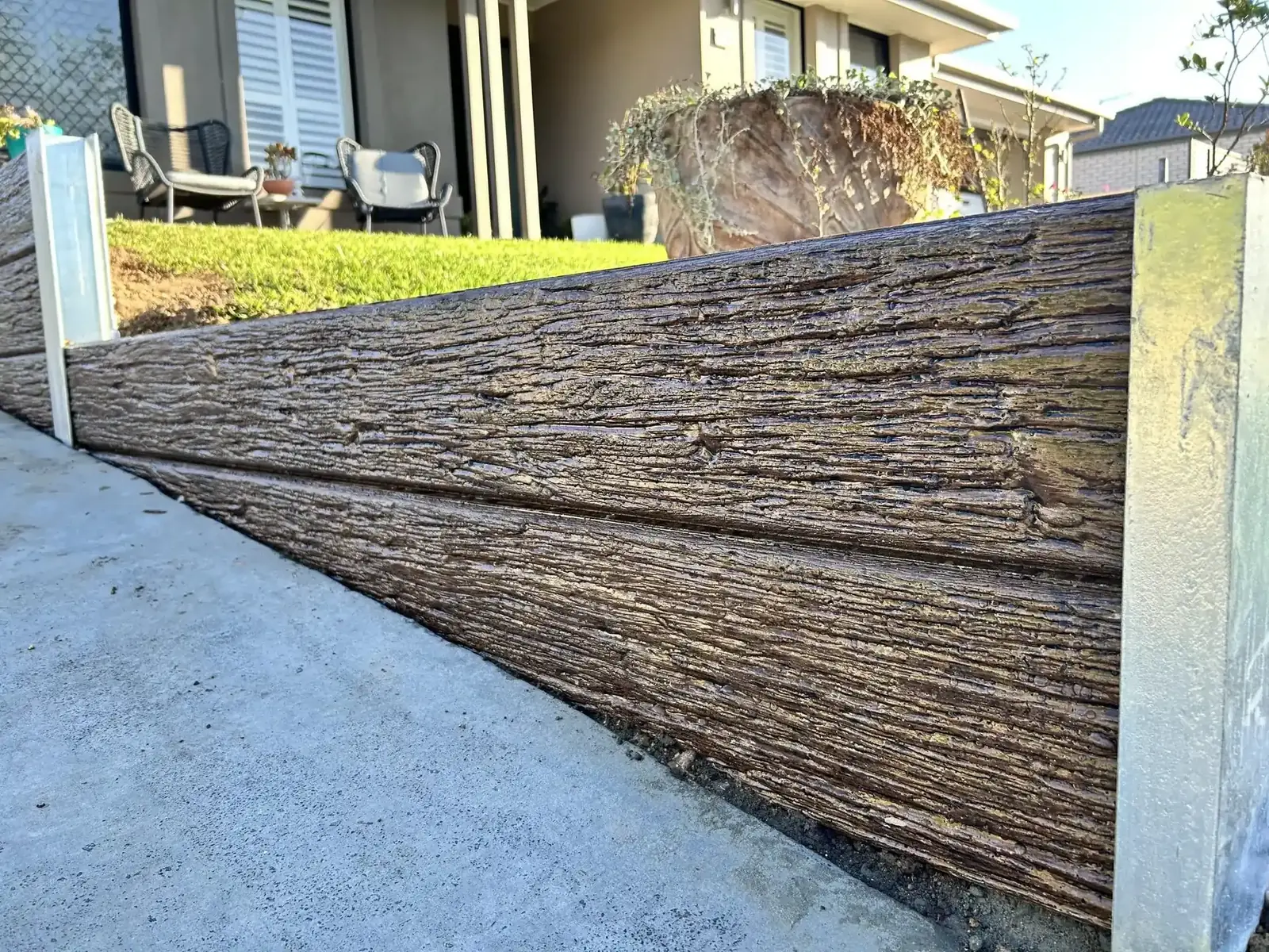 Close-up of a woodgrain concrete sleeper retaining wall beside a driveway