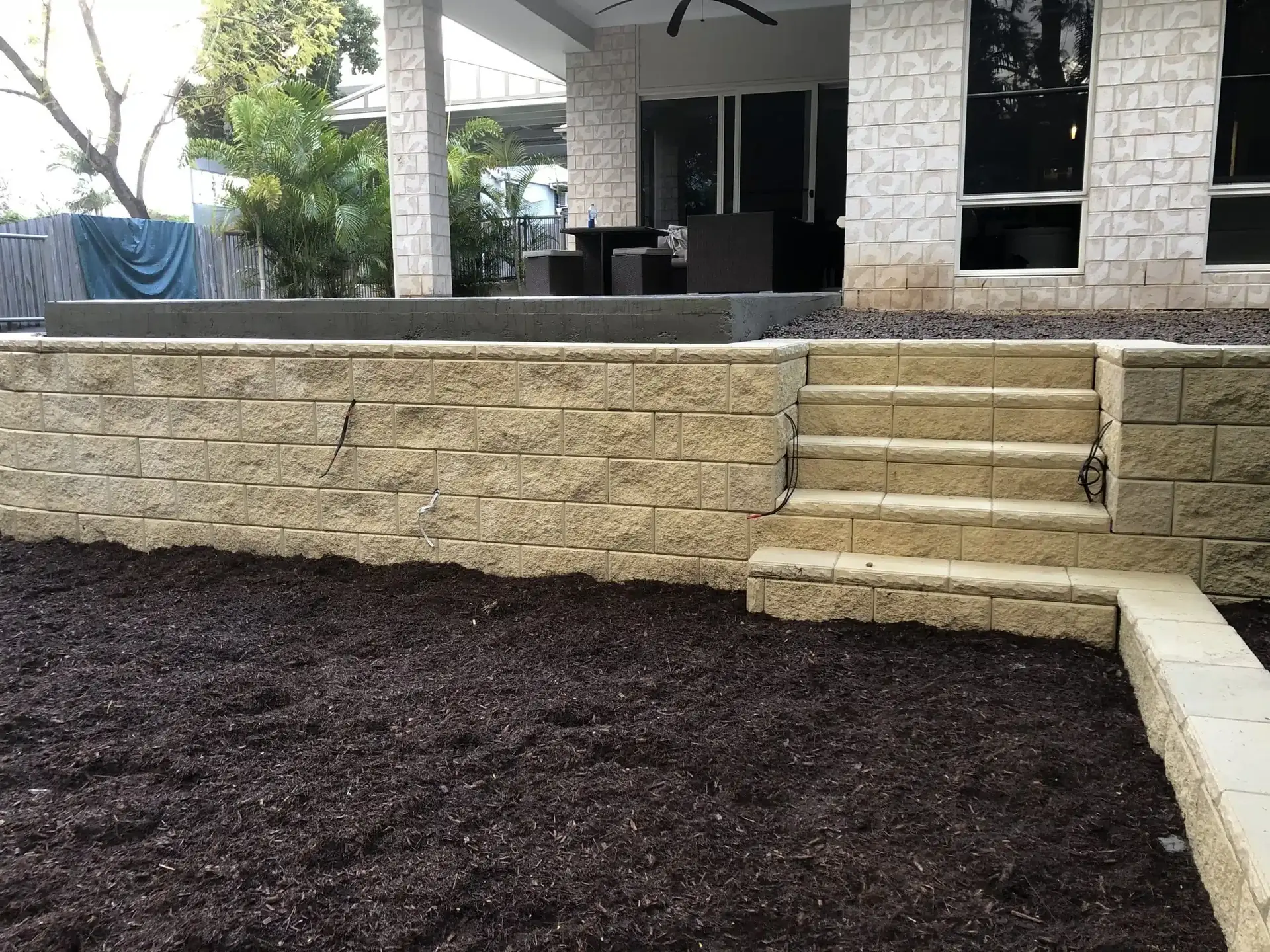Cream split-face block retaining wall with steps beside a new garden bed