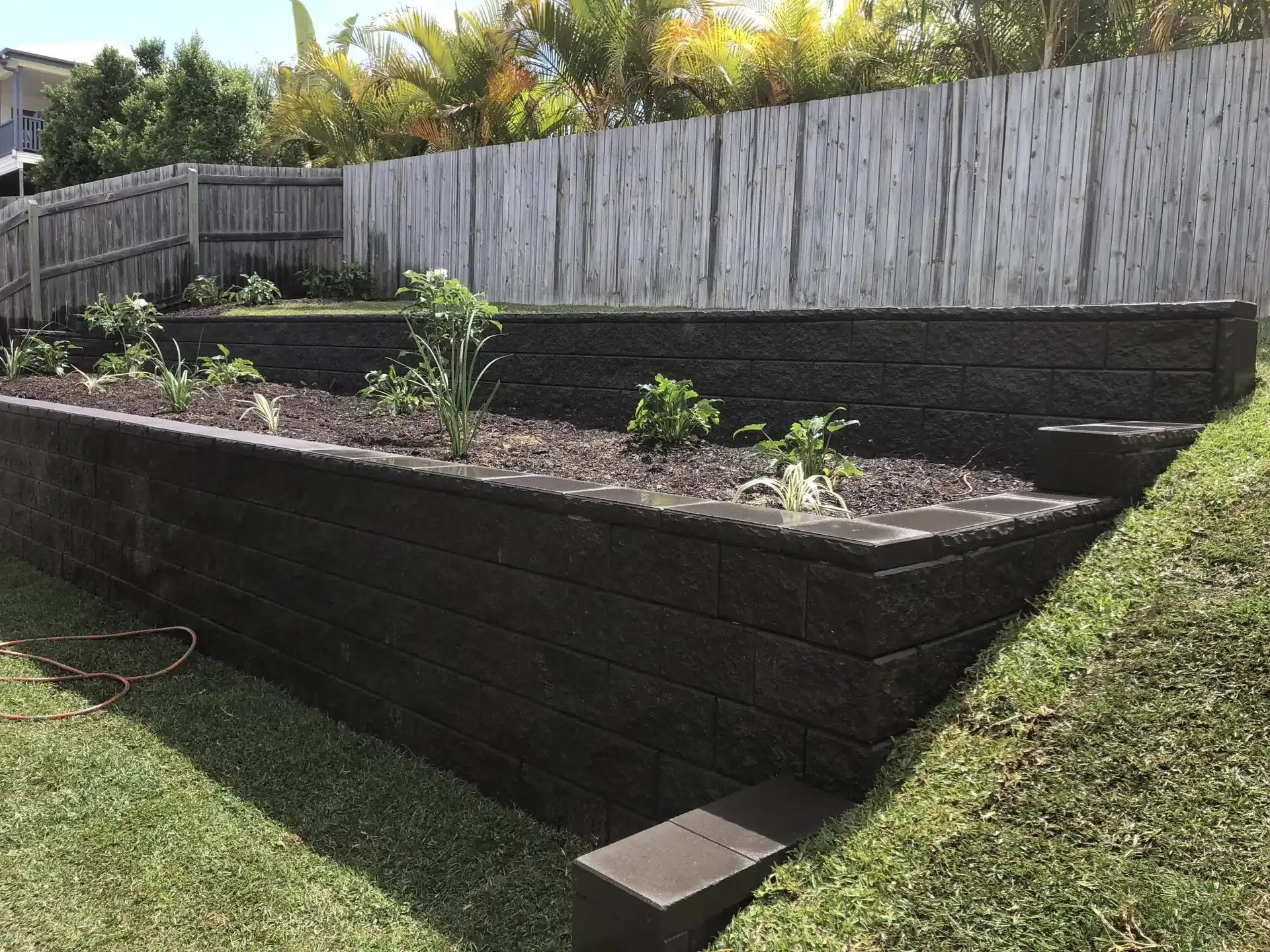 Charcoal block retaining wall around a newly planted garden bed below a timber fence