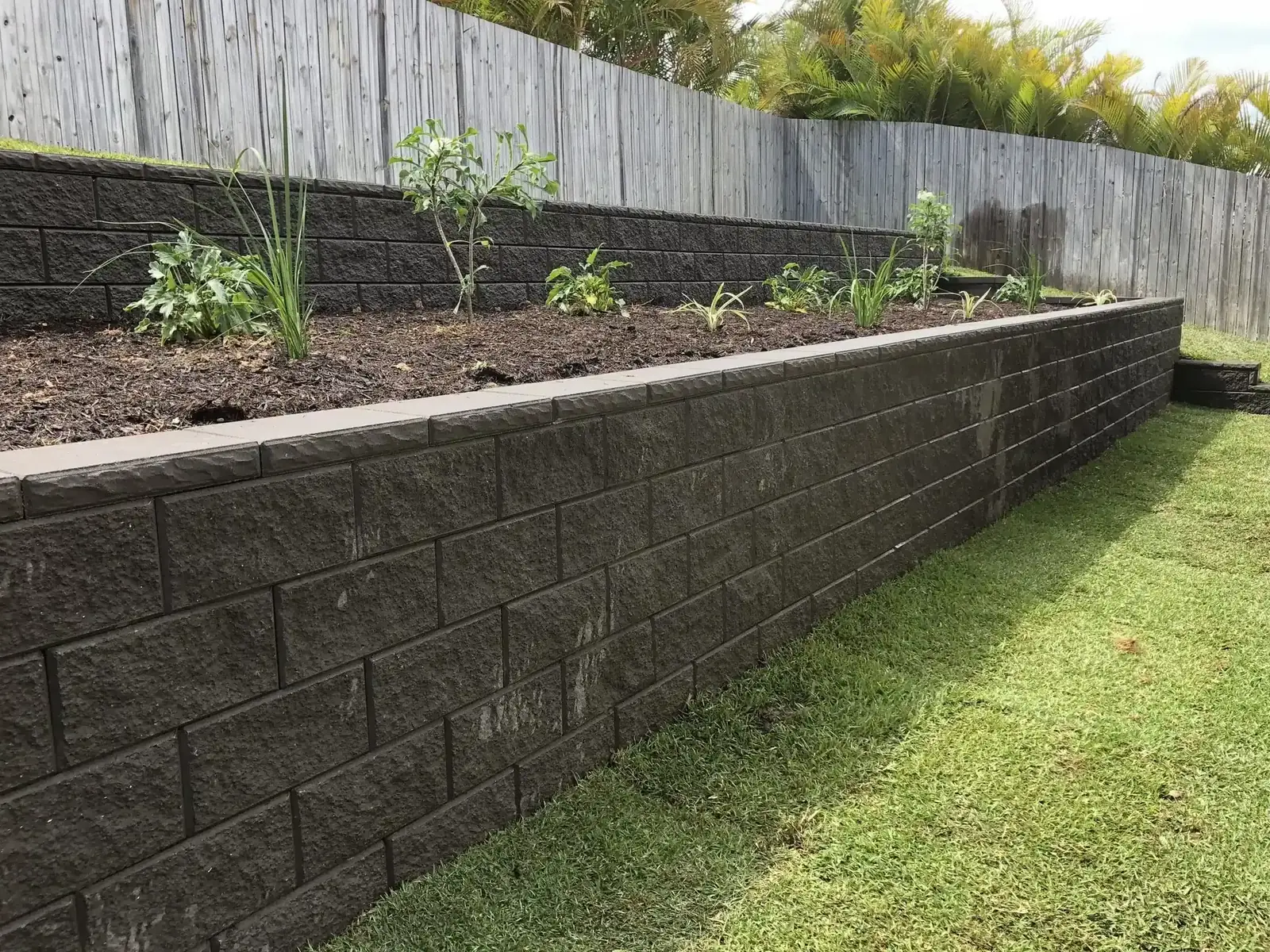 Charcoal block retaining wall edging a raised garden bed above a lawn