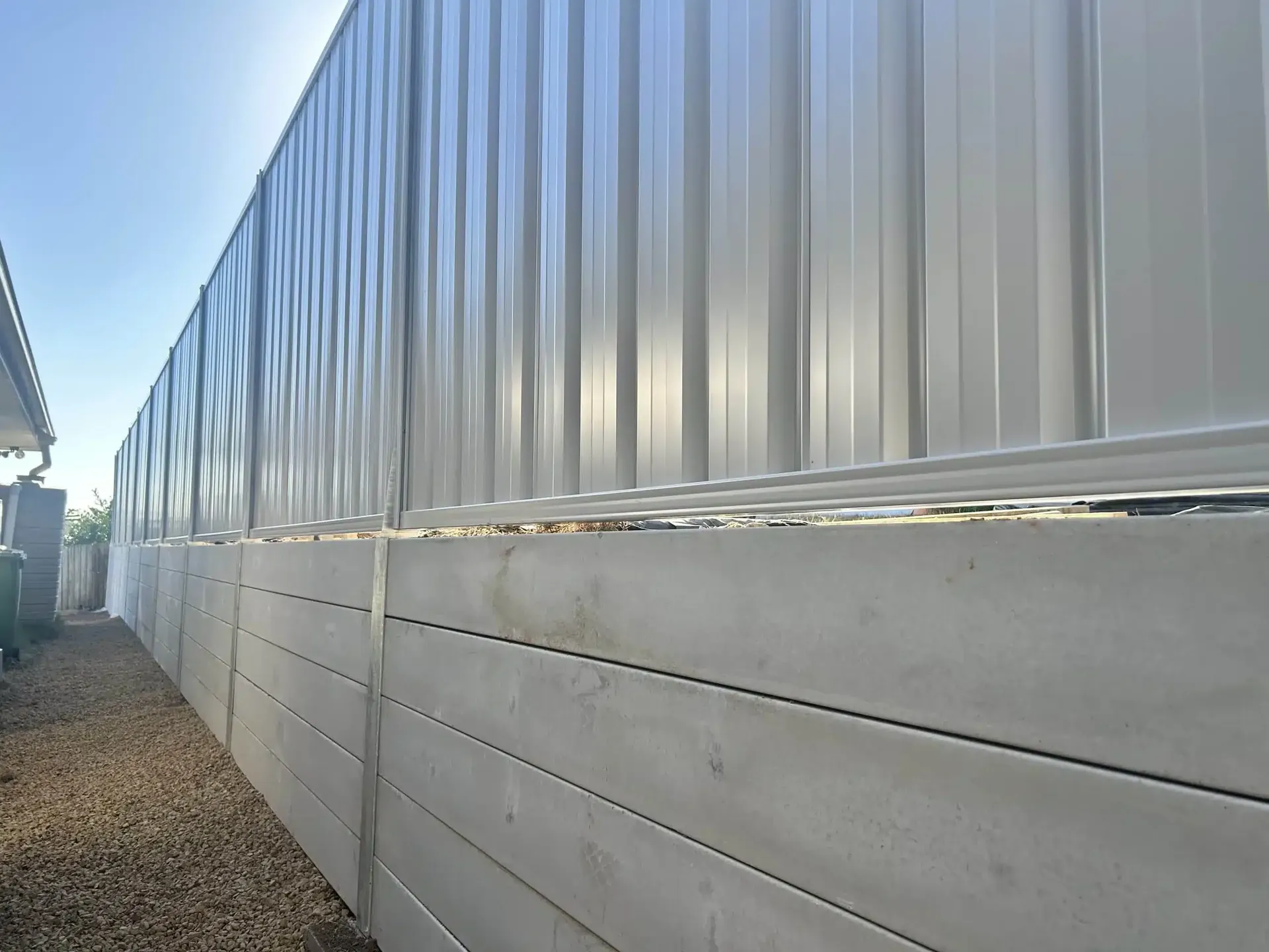 Smooth grey concrete sleeper retaining wall beneath a tall Colorbond fence