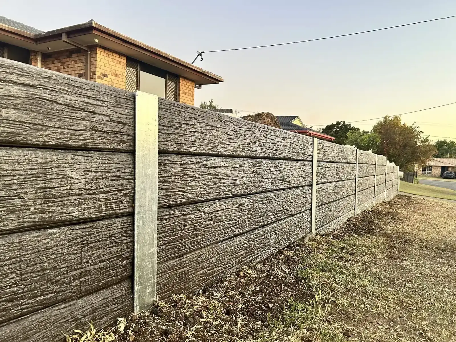 Woodgrain concrete sleeper retaining wall with galvanised posts along a front boundary