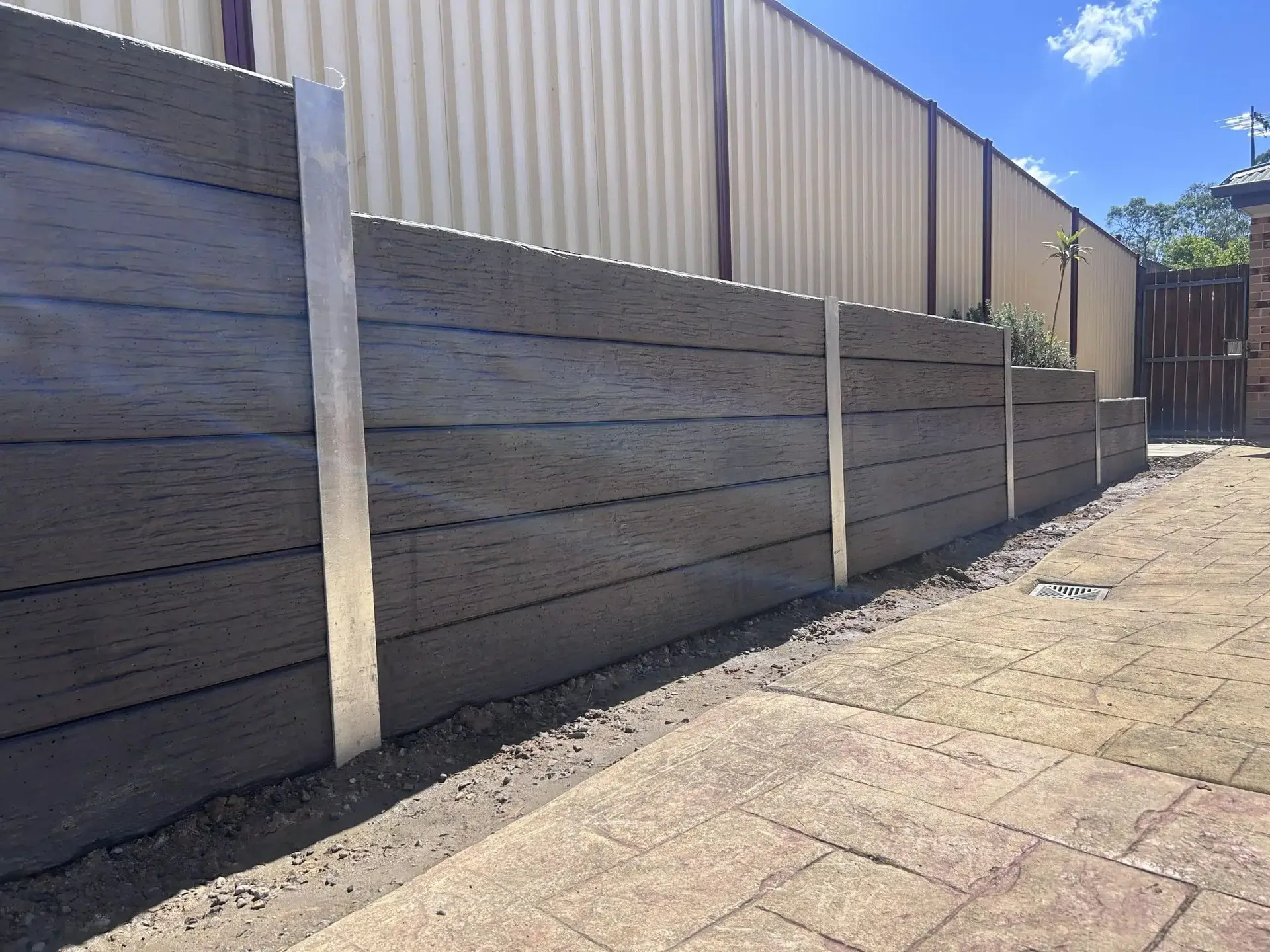 Grey concrete sleeper retaining wall with steel posts beside a paved side path