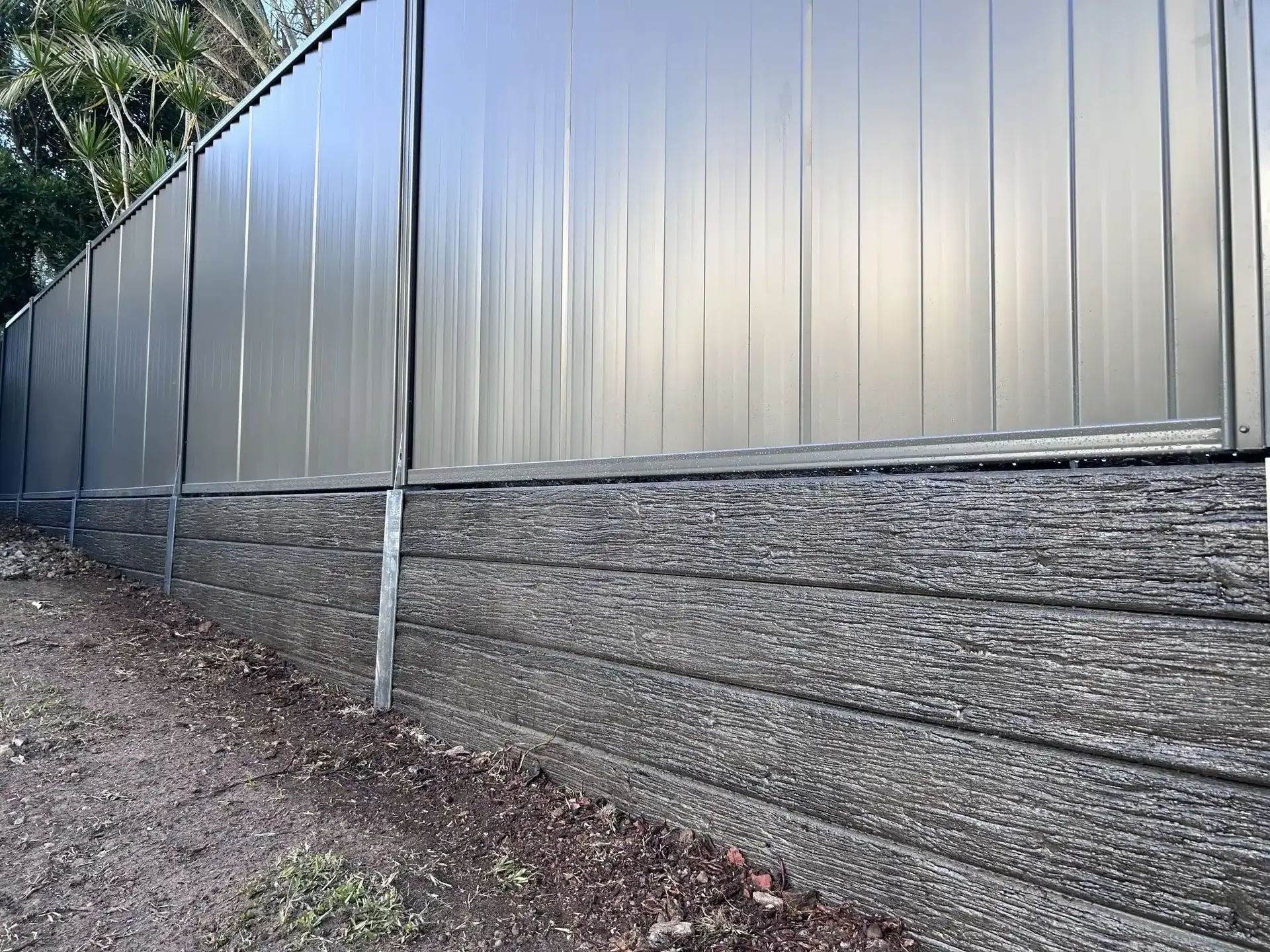 Rock-face concrete sleeper retaining wall beneath a grey Colorbond fence