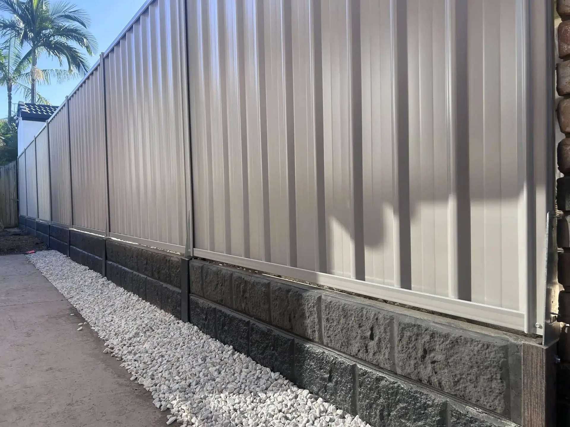 Charcoal concrete sleeper retaining wall with a white Colorbond fence above and gravel drainage