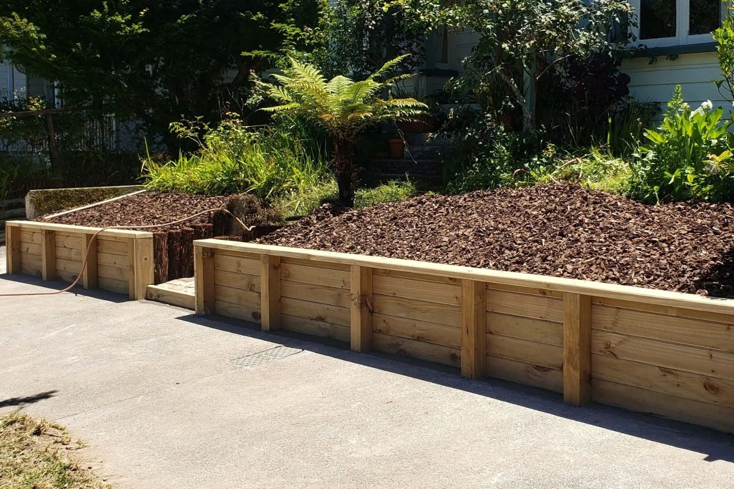 Treated timber retaining wall edging a mulched garden bed beside a concrete driveway