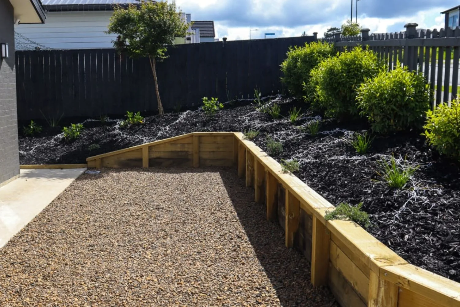 Timber edging retaining a planted garden bed beside a gravel area